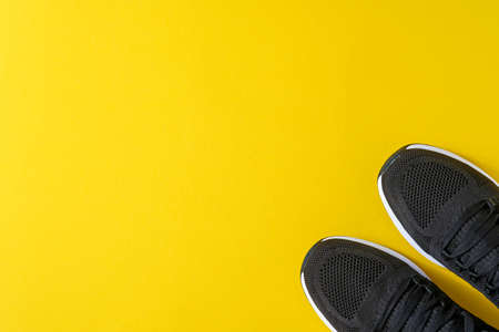 Black men sneakers on yellow background. Fashion blog or magazine concept. Men shoes, trendy sneakers, fashion, lifestyle. Mock up. Flat top view copy space minimal background.の写真素材