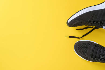 Black men sneakers on yellow background. Fashion blog or magazine concept. Men shoes, trendy...