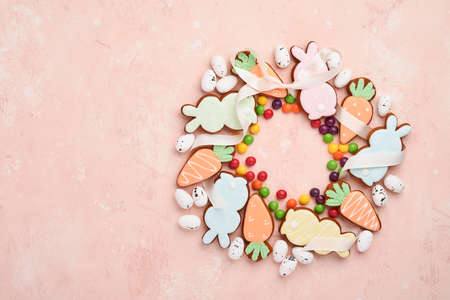 Easter eggs, cookie and colorful sweet made in shape of circle wreath on pink background. Minimal...