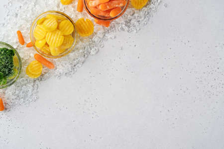 Frozen vegetables such as green broccoli, yellow and baby carrot in glass bowls on ice and concrete...