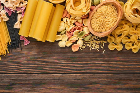 Variety of traditional italian pasta: colorful spaghetti, tagliatelle, farfalle, penne, ptititm, noodle, fusilli, cannelloni on an old wooden background. Top view with copy space.の写真素材