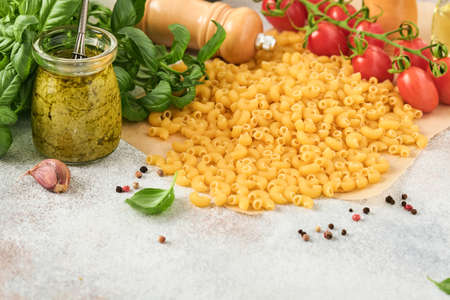 Chifferi rigati classic raw pasta in brown paper on light wooden table background with basil and...