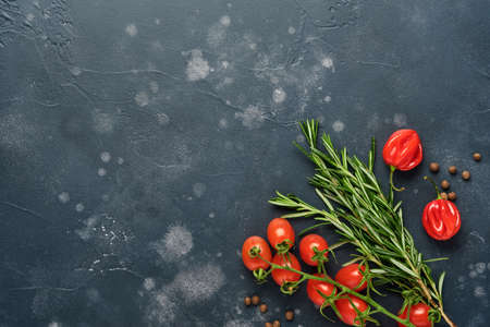 Food cooking background. Fresh rosemary, cilantro, basil, cherry tomatoes, peppers and olive oil, spices herbs and vegetables at black slate table. Food ingredients top view.の写真素材