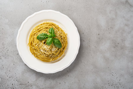 Pasta spaghetti with pesto sauce and fresh basil leaves in white bowl. Gray background. Mock up. Top view.の写真素材