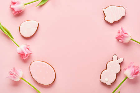 Easter greeting card with easter gingerbread eggs and tulip flowers over pink background. Top view flat lay with copy spaceの写真素材