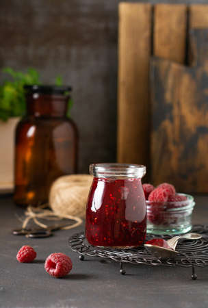 Raspberry jam in a glass jar with fresh raspberry berries on the old retro background.の写真素材
