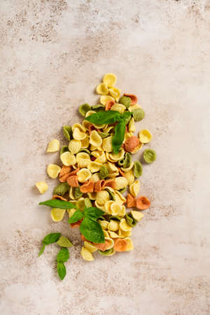 Raw orecchiette with parmesan cheese and tomatoes, basil with garlic and oil on light background with pepper on light brown background. Traditional ingredients for the preparation of Italian pasta.の写真素材