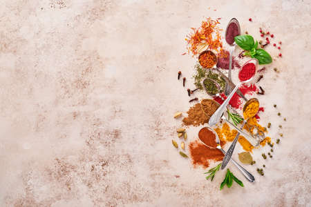 Colorful herbs and spices for cooking: turmeric, dill, paprika, cinnamon, saffron, basil and rosemary in a spoon. Indian spices. On light brown stone background. Top view.の写真素材