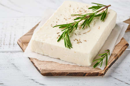 Cheese feta with rosemary, herbs and olive oil on wooden cutting board on white old wooden background. Traditional Greek homemade cheese. Selective focus.の写真素材