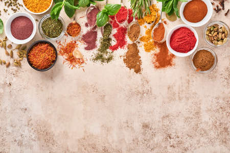 Colorful herbs and spices for cooking: turmeric, dill, paprika, cinnamon, saffron, basil and rosemary. Indian spices. On light brown stone background. Top view.の写真素材