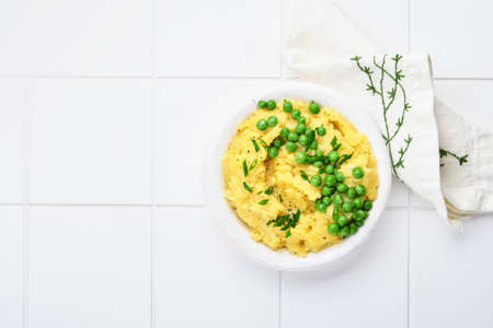 Mashed potato with butter, green peas, onions, basil on white ceramic tile background. Top view with close up.の写真素材