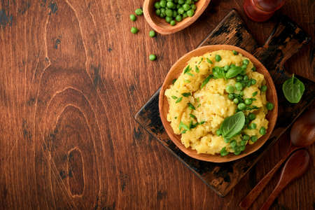 Mashed potato with butter, green peas, onions, basil on a rustic wooden background. Top view with close up.の写真素材