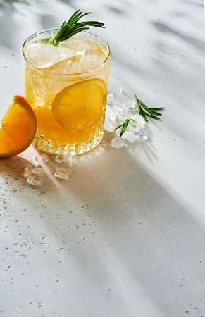 Orange juice or cocktail with rosemary and orange with ice in glass, cold summer lemonade on light gray slate, stone or concrete background. Beach concept with deep sun shadow. Top view.の写真素材
