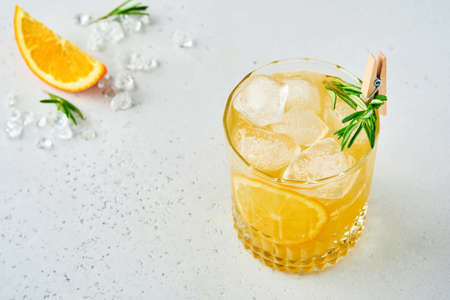 Orange juice or cocktail with rosemary and orange with ice in glass, cold summer lemonade on light gray slate, stone or concrete background. Beach concept with deep sun shadow. Top view.の写真素材