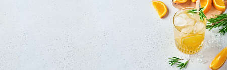 Orange juice or cocktail with rosemary and orange with ice in glass, cold summer lemonade on light gray slate, stone or concrete background. Beach concept with deep sun shadow. Top view.の写真素材