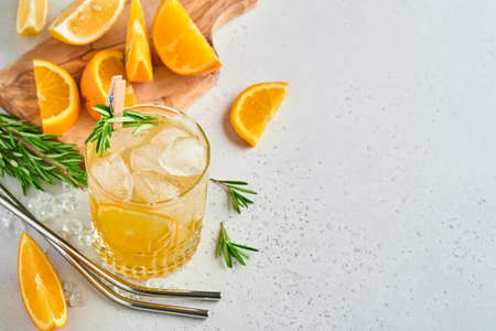 Orange juice or cocktail with rosemary and orange with ice in glass, cold summer lemonade on light gray slate, stone or concrete background. Beach concept with deep sun shadow. Top view.の写真素材