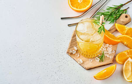 Orange juice or cocktail with rosemary and orange with ice in glass, cold summer lemonade on light gray slate, stone or concrete background. Beach concept with deep sun shadow. Top view.の写真素材