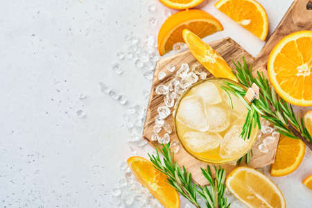 Orange juice or cocktail with rosemary and orange with ice in glass, cold summer lemonade on light gray slate, stone or concrete background. Beach concept with deep sun shadow. Top view.の写真素材
