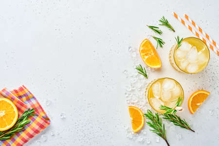 Orange juice or cocktail with rosemary and orange with ice in glass, cold summer lemonade on light gray slate, stone or concrete background. Beach concept with deep sun shadow. Top view.の写真素材