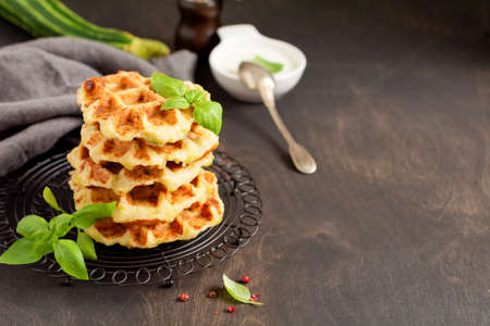 Homemade zucchini waffles stack with cheese, sause and leaf basil on old wooden dark background. Concept of keto diet food. Selective focusの写真素材
