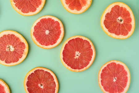 Grapefruit citrus pattern composition. Grapefruit slices with juice are scattered around on a green background with shadows. Summer or spring concept. Mock up. Top view.の写真素材