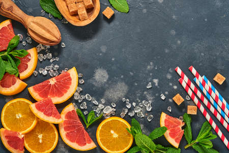 Grapefruit and orange slices, mint, cane sugar, ice, cocktail tubes, juicer or squeezer on black stone old background. Ingredients for making summer beach cocktail drink background. Mock up. Top view.の写真素材