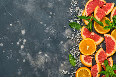 Grapefruit and orange slices, mint, cane sugar, ice, cocktail tubes, juicer or squeezer on black stone old background. Ingredients for making summer beach cocktail drink background. Mock up. Top view.の写真素材