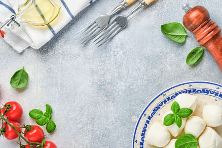 Mozzarella cheese with basil in white ceramic plate, tomato cherry olive oil and spice grinder, condiments, pepper tomato cherry on slate stone background. Mock up. Ingredients for Caprese salad.の写真素材