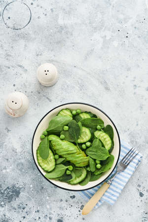 Green vegetable salad with spinach, avocado, green peas and olive oil in bowl on light gray slate, stone or concrete background. Top view with copy space. Green vegetables for diet concept.の写真素材