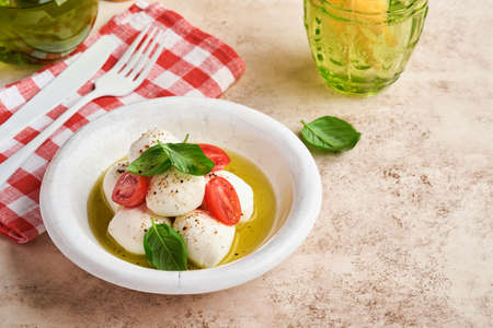 Caprese salad. Mozzarella cheese with basil and cherry tomato in white ceramic plate and tomato...