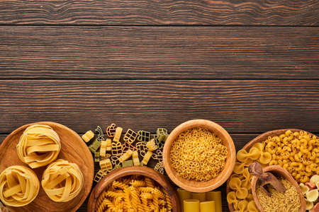 Variety of traditional italian pasta: colorful spaghetti, tagliatelle, farfalle, penne, ptititm, noodle, fusilli, cannelloni on an old wooden background. Top view with copy space.の写真素材