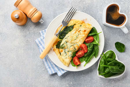 Omelet or omelette with spinach, cherry tomato and pepper seasoning on a white plate, on light gray background. Healthy breakfast concept. Top view.の写真素材
