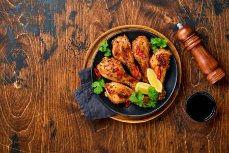 Grilled chicken drumsticks or legs or roasted bbq with spices and tomato salsa sauce on a black plate on old wooden background. Top view with copy space.の写真素材