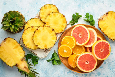 Sliced ripe pineapple, orange and grapefruit on light blue stone background. Tropical fruits. Top view. Free space for text. Mock up.の写真素材