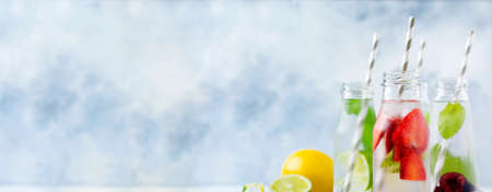 Bottles lemonade refreshing summer lemonade with lime, strawberry, cherry, cucumber and ice on a gray concrete background. Mock up.の写真素材