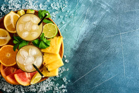 Fresh juice pineapple with ice and variety sliced ripe of color tropical fruits grapefruit, orange, lime, lemon, flat lay composition, on dark blue stone background. Mock up.の写真素材