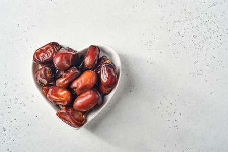 Dried sliced date fruit in a heart-shaped ceramic plate on white background with copy space. Snack vegan sugarfree food.の写真素材