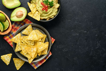 Guacamole. Traditional latinamerican Mexican dip sauce in a black bowl with avocado and ingredients and corn nachos. Avocado spread. Top view. Copyspaceの写真素材