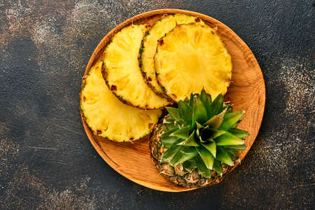 Sliced ripe pineapple on dark brown stone background. Tropical fruits. Top view. Free space for text. Mock up.の写真素材