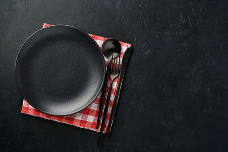 Black empty plate, fork and knife and red tablecloth. Kitchen utensils set on black stone table. Top view. Mock up.の写真素材