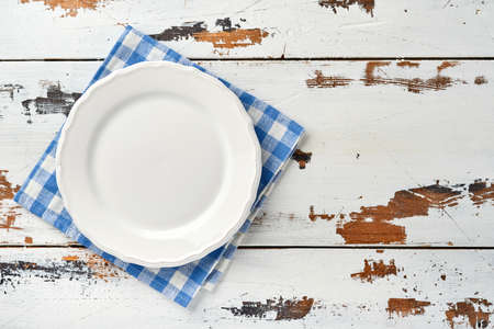 Empty white plate and blue towel over old white wooden table background for your recipe or menu. Top view. Mock up.の写真素材