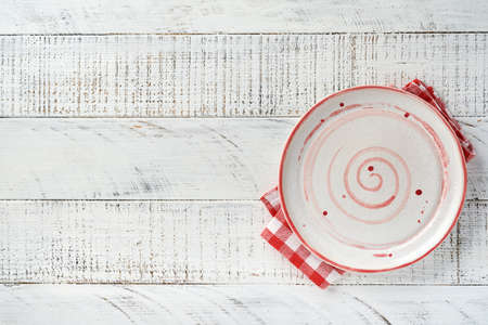 Empty white plate and red towel over old white wooden table background for your recipe or menu. Top view. Mock up.の写真素材