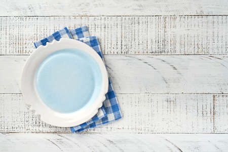Empty white plate and blue towel over old white wooden table background for your recipe or menu. Top view. Mock up.の写真素材