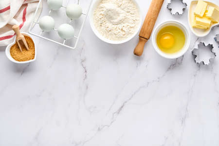 Baking background with flour, eggs, kitchen tools, utensils and cookie molds on white marble table. Top view. Flat lay style. Mock up.の写真素材