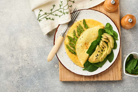 Omelette or omelet stuffed with asparagus, avocado and spinach leaves for breakfast on white plate over white slate, stone or concrete background. Balanced and tasty morning food. Mock up. Top view.の写真素材