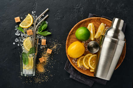 Mojito or Lemonade cocktail in highball glass with ice cubes, mint and lime on black stone background with shaker and beaker. Menu bar. Space for text. Top view.の写真素材