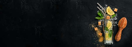 Mojito or Lemonade cocktail in highball glass with ice cubes, mint and lime on black stone background with shaker and beaker. Menu bar. Space for text. Top view.の写真素材