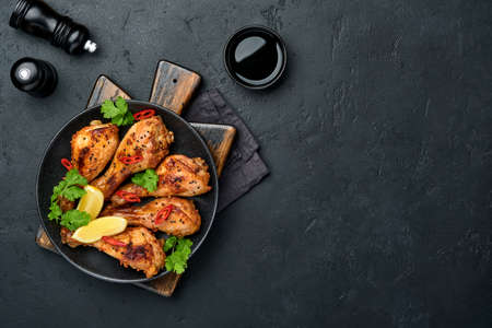 Grilled chicken drumsticks or legs or roasted bbq with spices and tomato salsa sauce on a black plate. Top view with copy space.の写真素材