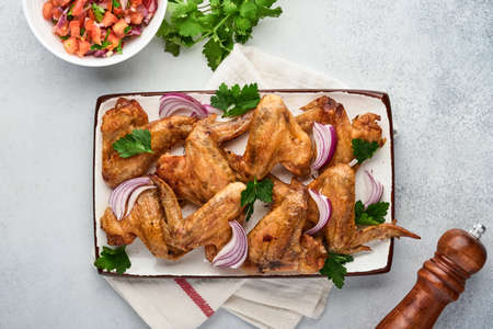 Grilled chicken wings or roasted bbq with spices and tomato salsa sauce on plate on a light gray slate, stone or concrete background. Top view with copy space.の写真素材