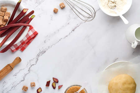 Ball of dough and ingredients flour, water, butter, sugar and rhubarb for baking on white marble...